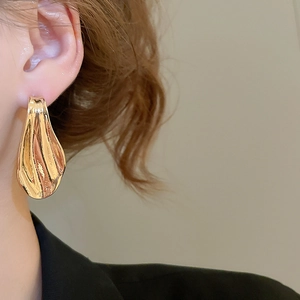 Close-up of golden irregular waterdrop earrings featuring a modern metallic wrinkled design