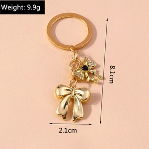 Detailed view of golden double bow keychain with black gem and product dimensions