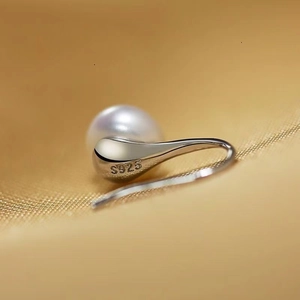 Close-up of the S925 silver hallmark on a pearl ear hook against soft fabric