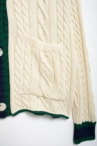 Close-up of cream cable knit cardigan featuring contrast stripes and white buttons