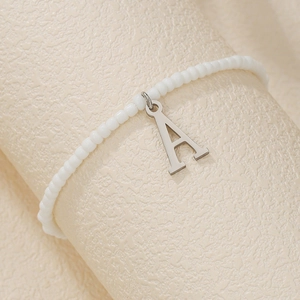 Detail of white seed bead anklet with a silver letter A pendant on beige texture