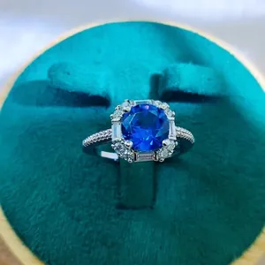 Close-up of a silver halo ring with a large blue gemstone in a green velvet box