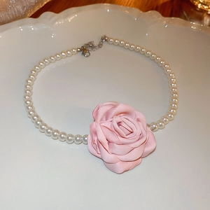 Vue détaillée d'un pendentif rose en tissu sur un collier de perles dans un plat vintage