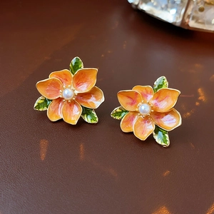 Detailed view of orange enamel flower earrings with white pearl center and green leaf accents