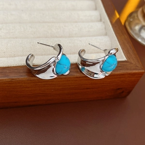 Detail of silver C-shaped earrings with blue turquoise inlay on a wooden jewelry box