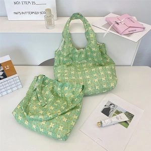 Detail of green floral tote bag with daisy prints and a brand label on white surface