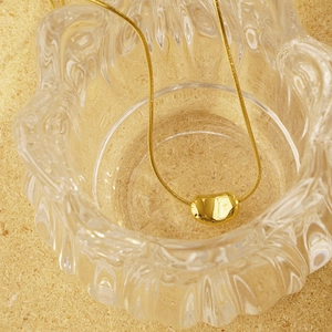 Elegant gold bean pendant necklace with minimalist snake chain over rustic wooden chips