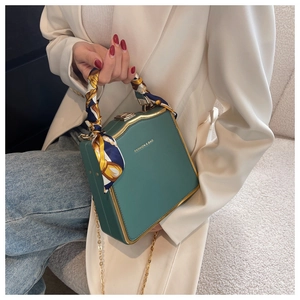 Detail of dark green square box bag with silk scarf handle and gold chain strap