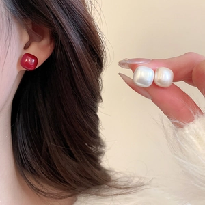 Macro detail of minimalist square stud earrings in red and white on a soft knit sweater