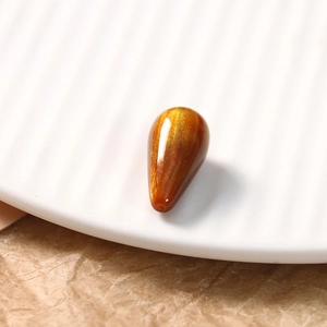Macro view of teardrop resin bead in golden brown with shimmering cat-eye effect