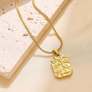 Close-up of golden rectangular pendant with hammered texture on elegant snake chain