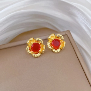 Close-up of golden flower stud earrings with red crystal center on a beige jewelry box