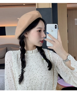 Detailed view of a beige wool beret paired with a white floral long-sleeve blouse