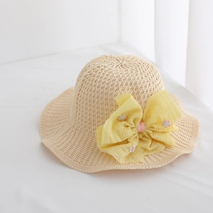 Detailed macro view of a children's beige straw sun hat featuring a large yellow fabric bow.