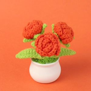 Detailed view of hand-crocheted orange roses in a white ceramic pot with green leaves