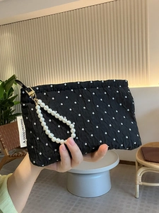 Close-up of black polka dot quilted clutch with elegant pearl handle and brand label