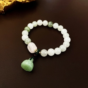 Detail of beaded bracelet with light green jade beads and a green bell pendant