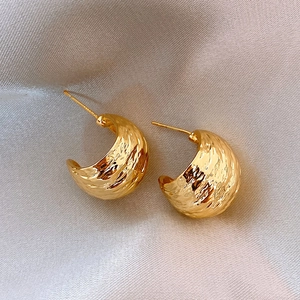 Macro detail of golden hammered texture earrings displayed on soft silk fabric folds