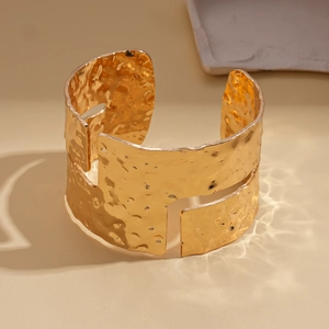 Close-up of golden wide cuff bracelet featuring unique hammered texture and hollow design