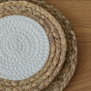 Close-up of stacked round woven placemats with dual-color cotton rope and natural grass fiber