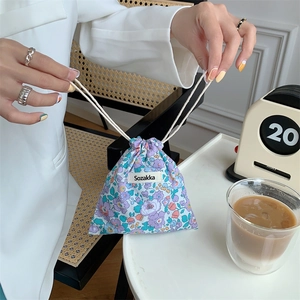 Floral fabric drawstring pouch held by hand, showing portable size and texture details