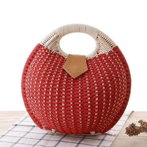 Red circular straw handbag with white handles on a rustic table in summer style