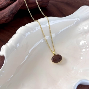 Macro shot of minimalist deep red bean pendant on golden chain over white ceramic dish