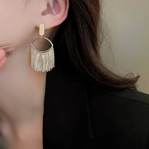 Macro view of gold-plated oval earrings featuring delicate long metal fringe tassels