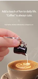 Miniature black milk pitcher keychain with metal ring shown against latte coffee