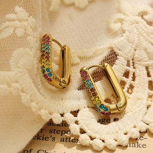 Macro detail of gold U-shaped earring with colorful rhinestones on vintage lace and book background