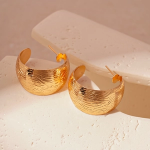 Vue détaillée des boucles d'oreilles dorées en C avec texture métallique ondulée martelée