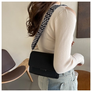 Detail of a black square bag featuring a unique geometric textured wide shoulder strap