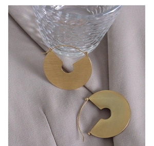 Detail of gold brushed texture hoop earrings displayed on soft fabric with glass backdrop