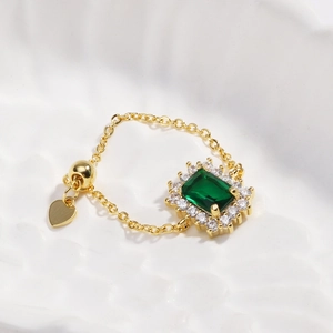 Detail of adjustable gold chain ring with emerald green stone and heart charm