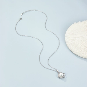 Macro detail of silver necklace featuring a round white pearl pendant on a blue background
