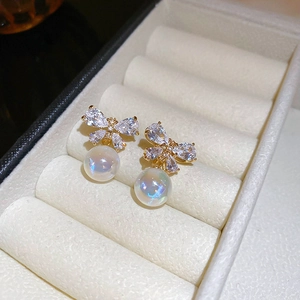 Close-up of golden butterfly earring with cubic zirconia and iridescent pearl drop