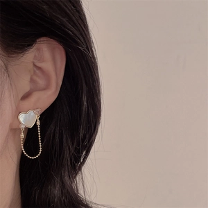 Close-up of gold heart earrings with white mother of pearl and delicate pearl tassels
