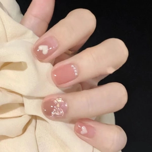 Close-up of handmade press-on nails featuring pink bows, white hearts, and small pearls