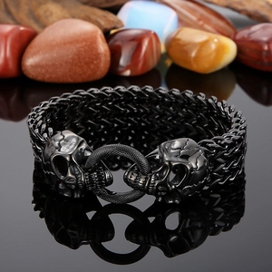 Detail of a black woven metal punk bracelet featuring a double skull head clasp design
