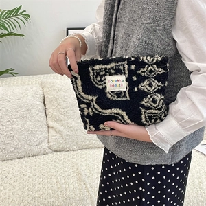 Close-up of fluffy black and white abstract textured plush makeup bag with woven label