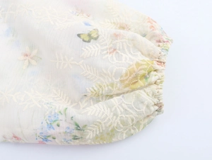 Détail de la manche lanterne brodée avec imprimé floral et papillon sur tissu crème