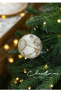 Close-up of white foam Christmas ball with gold glitter swirls hanging on a tree