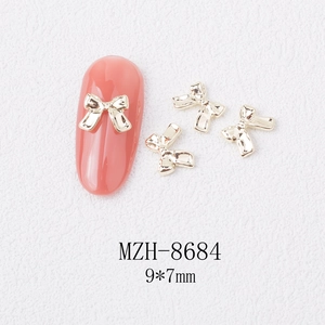 Macro detail of 9x7mm golden alloy bow nail art charm with metallic texture and dimensions