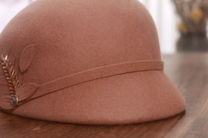 Macro detail of wool cloche hat with floral metal buckle and leaf embroidery