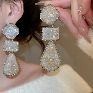 Macro detail of geometric resin drop earrings with gold foil flakes and wavy metal trim