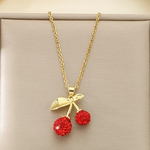 Macro detail of gold cherry pendant necklace featuring pavé red crystals and shiny leaves