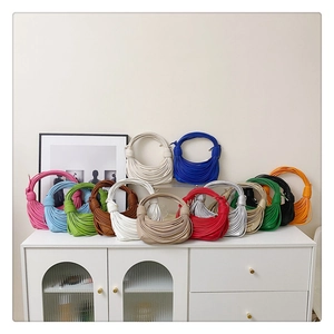 Various colors of knotted half-moon shoulder bags displayed on a minimalist white cabinet
