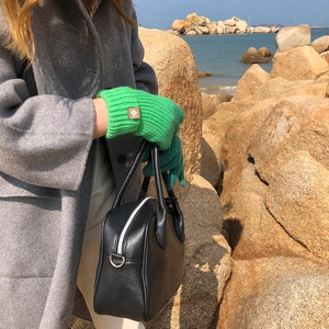 Outdoor shot of green knitted gloves held against a grey wool coat and black leather bag