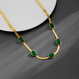 Collana vintage a serpente dorata con cinque pietre verdi smeraldo su piatto bianco
