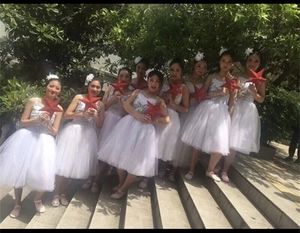 Group photo of dancers in white sequined tutu dresses holding red star ornaments
